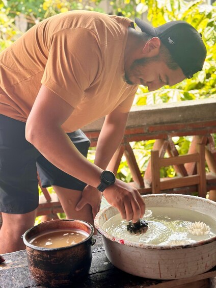 A person in a brown shirt and black shorts, wearing a cap, handling a fish in a large white bowl with a floral design. 3