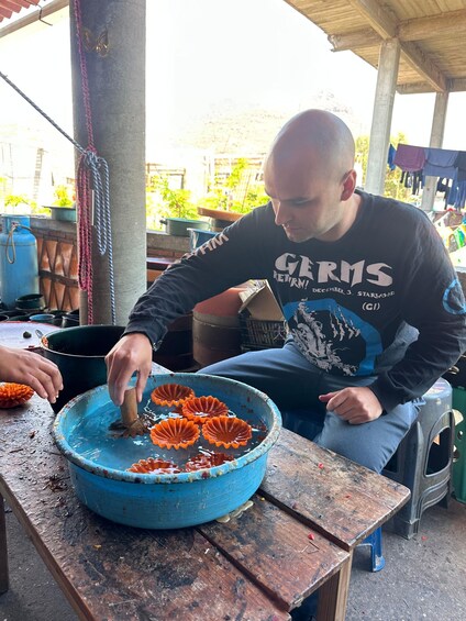 A person sitting at a wooden table, handling a blue bowl with orange objects. 2