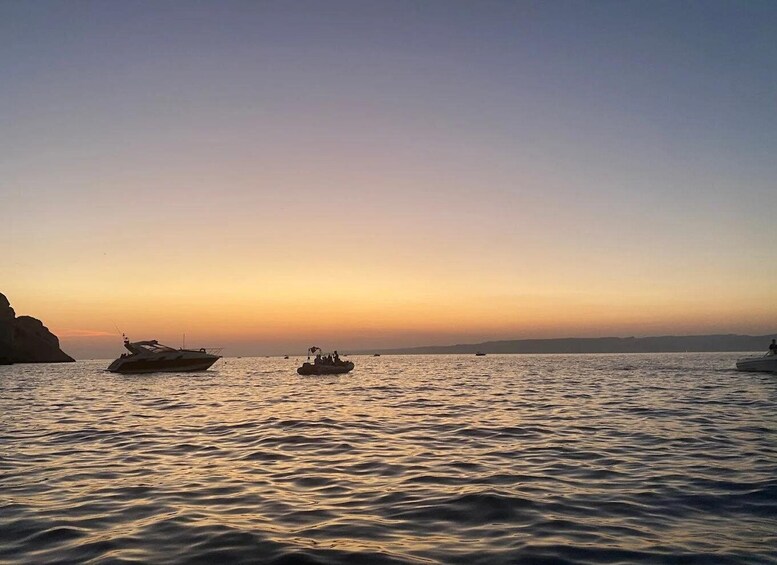 A calm sea at sunset with boats and a rocky coastline. 3