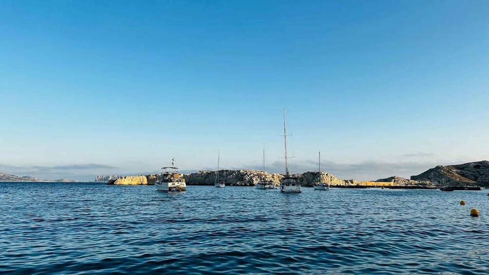 A calm sea with several sailboats anchored near rocky coastlines. 2