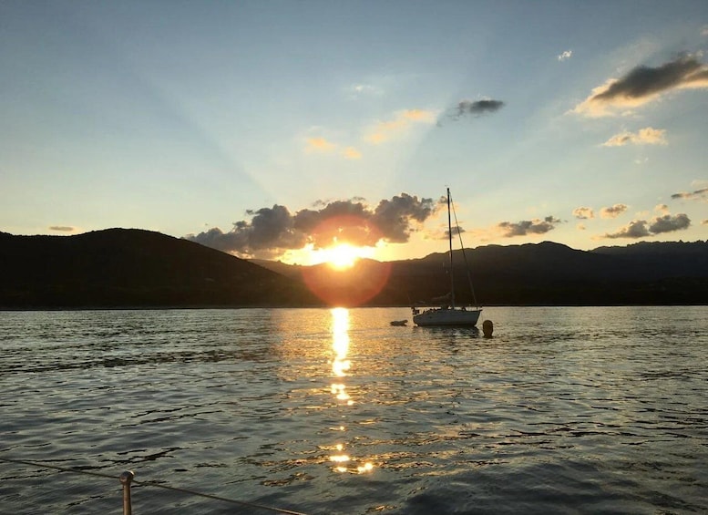 A sunset over a calm lake with a sailboat and a small motorboat. 1