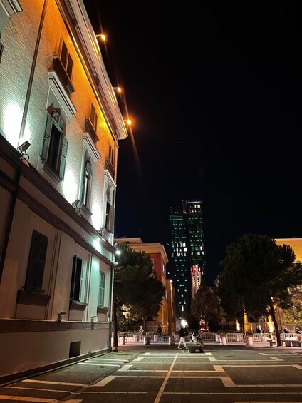A nighttime cityscape with illuminated buildings, a crosswalk, and a tall skyscraper in the background. 2