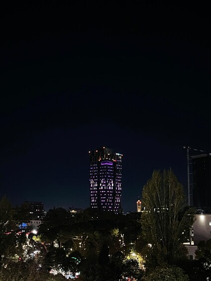 A nighttime cityscape with a brightly lit skyscraper and surrounding trees. 5