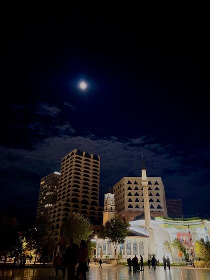 A night scene with a prominent building featuring a clock tower and a mosque with a minaret, under a moonlit sky. 1