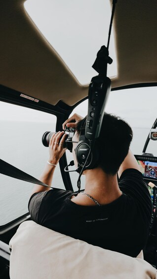 A person with a camera mounted on a tripod inside a vehicle, possibly a boat, with a view of the water outside. 2