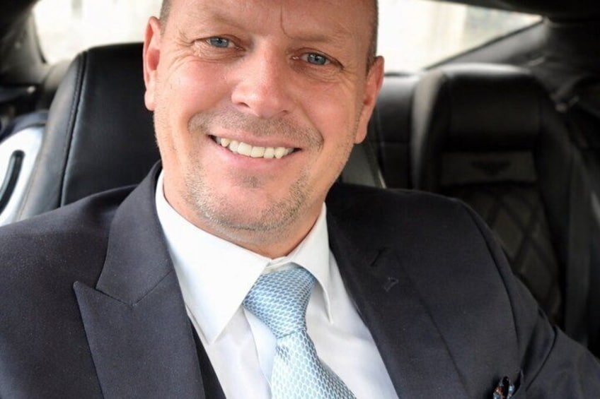A person in a car wearing a dark suit and a light blue tie. 2