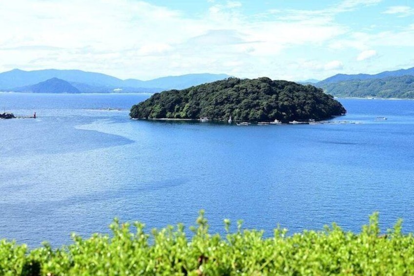 A large island surrounded by calm blue waters, with distant mountains under a clear sky. 3