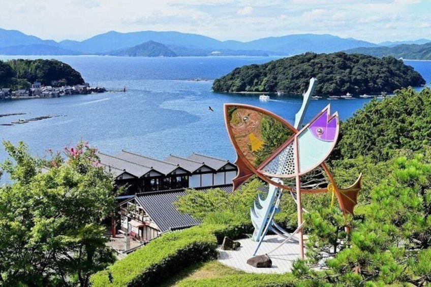 A scenic view of a lake with a traditional Japanese building and a colorful wind sculpture. 1