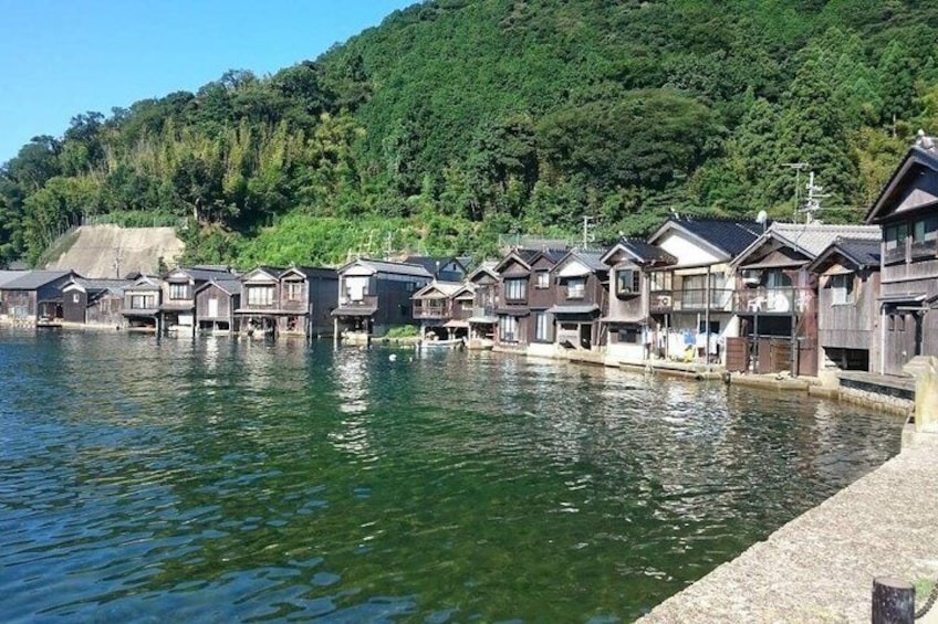 A row of wooden houses by a calm lake with a forested hill in the background. 5