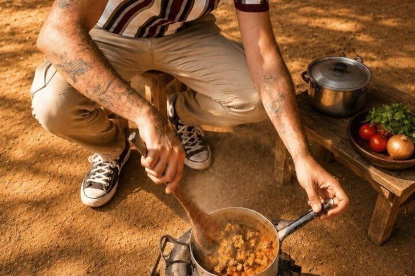 A person cooking outdoors, using a portable stove with a pot on it. 3