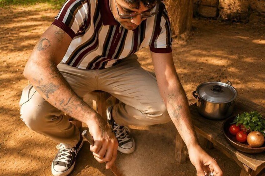 A person kneeling on the ground, preparing food outdoors with a pot and vegetables. 4