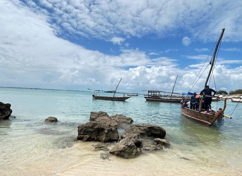 A beach with clear turquoise water, rocky shoreline, and several traditional boats anchored near the shore. 3