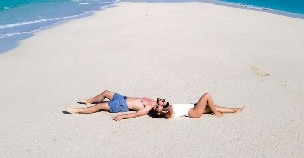 Two people lying on a sandy beach with a calm sea in the background. 3