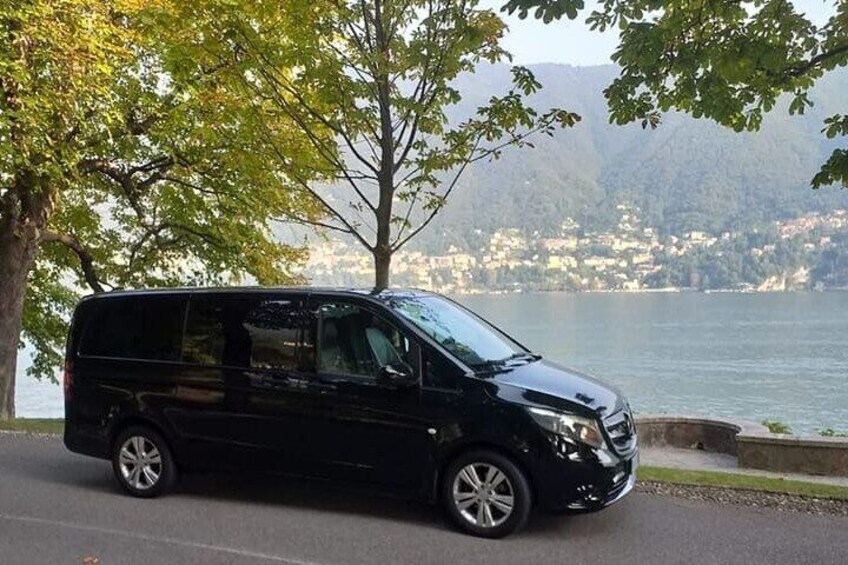 A black van parked on a road with a lake and mountains in the background. 3