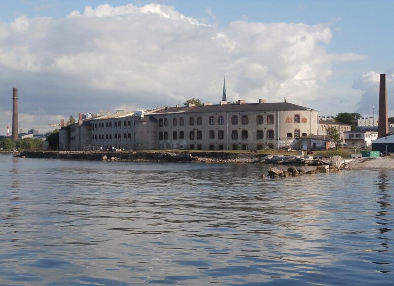 A historic building by a waterfront with a church steeple, industrial chimneys, and a calm river. 4