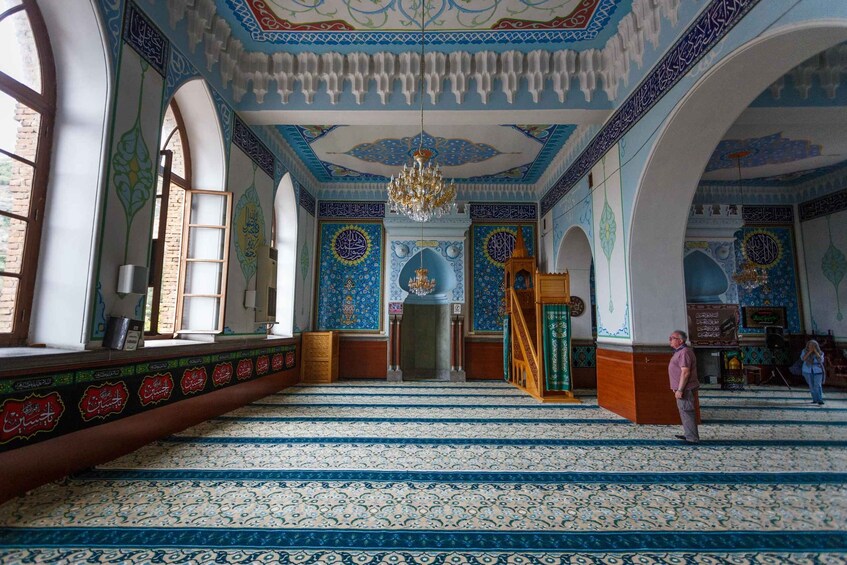 An ornate mosque interior with intricate tile work, a chandelier, and a minbar. 4