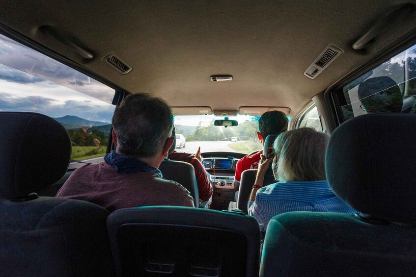 The interior of a car with four passengers, a dashboard, and a view of the road ahead. 1