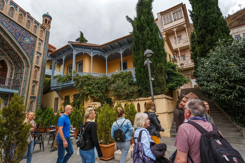 A courtyard with ornate architecture, a staircase, and people walking. 2