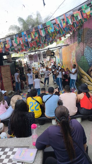 A street market with colorful flags, people shopping, and a mural on the wall. 3