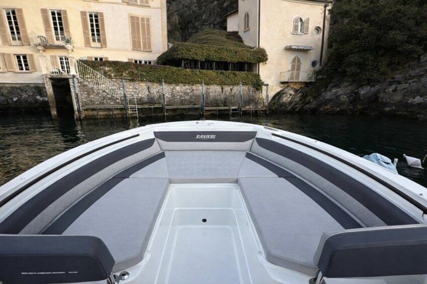 A boat with a white and gray interior, docked near a building with a stone wall and greenery. 2