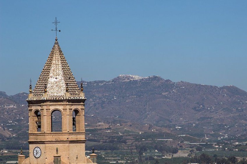 A bell tower with a clock, surrounded by a mountainous landscape. 3