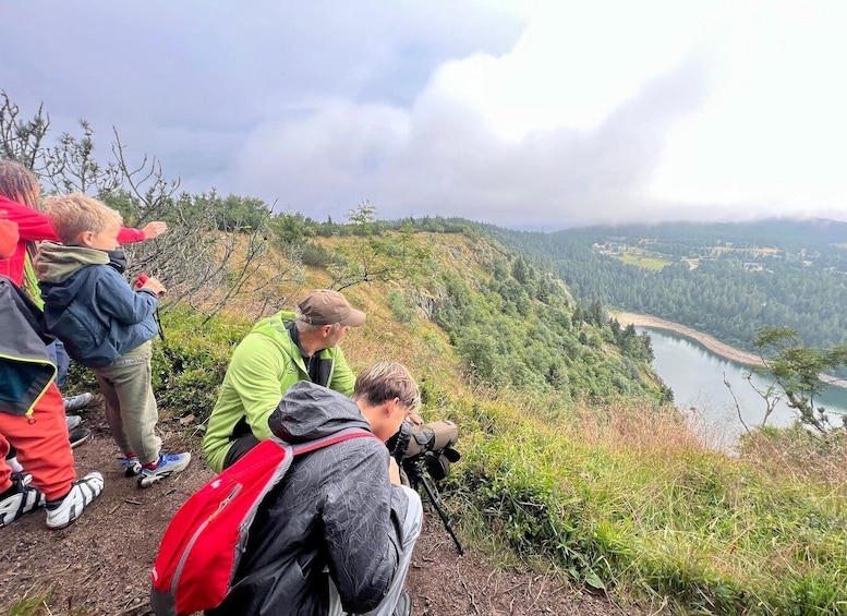 A group of people on a mountain trail overlooking a lake and forested valley. 2