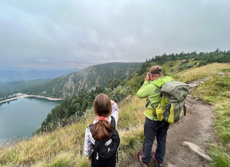 Two hikers on a mountain trail overlooking a lake and forested hills. 3