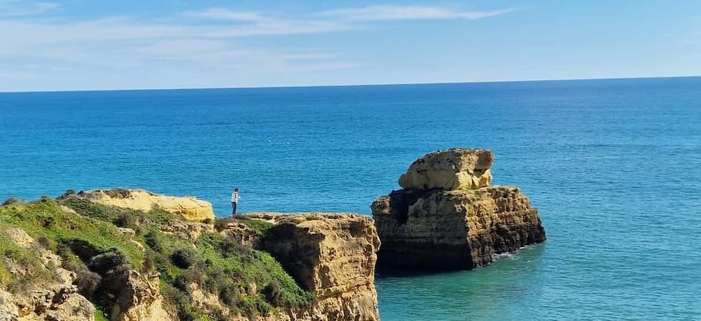 A coastal landscape with a person standing on a cliff overlooking the sea. 2