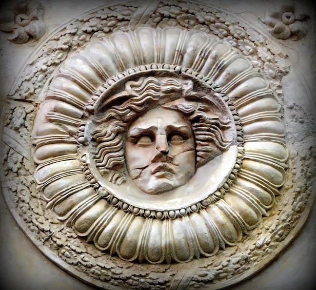 A detailed stone carving with a central face surrounded by ornate patterns. 1
