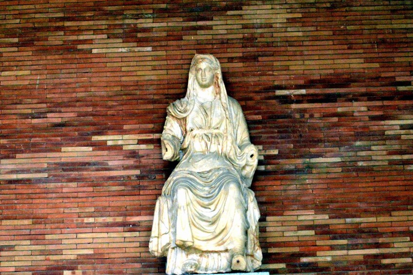 A stone statue of a seated figure against a brick wall. 3