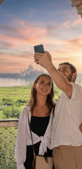 A person taking a selfie with a smartphone, another person standing beside them, and a scenic view of a large white dome structure in the background. 3