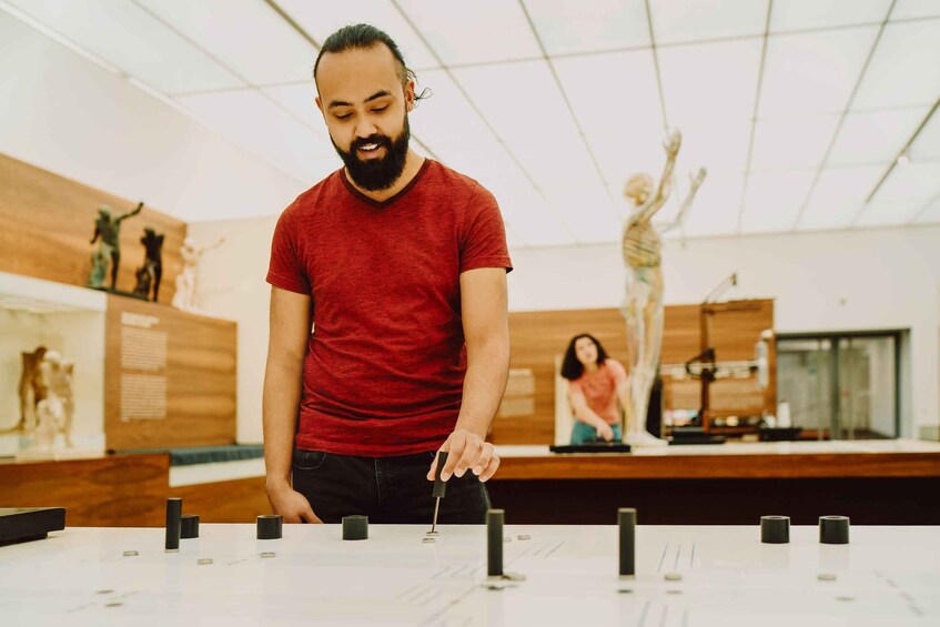 A person in a red shirt working with a device on a table in a room with wooden walls and a sculpture in the background. 1