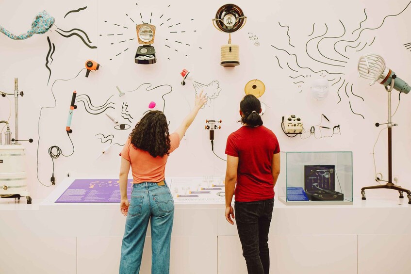 Two people observing an art installation with various objects and drawings on the wall. 5