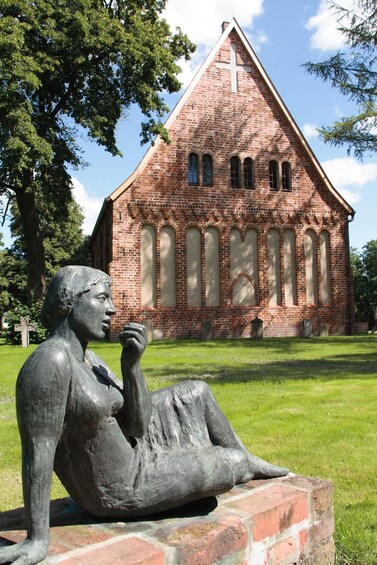 A statue of a woman sitting on a brick base, a brick church with a cross, and a cross in the background. 2