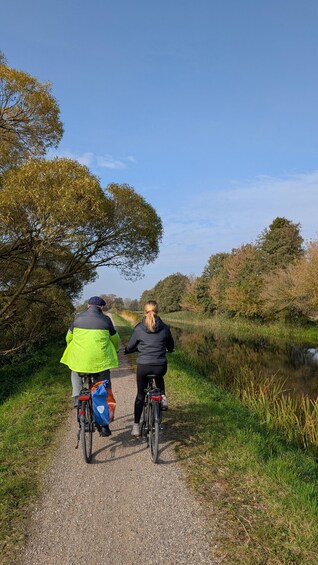 Two cyclists on a gravel path with a body of water and trees on one side. 3