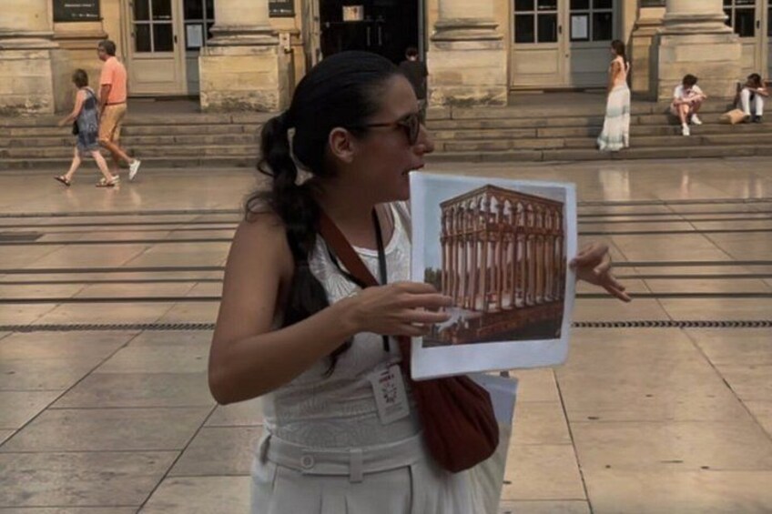 Una persona tiene in mano un libro con un'illustrazione di un edificio, in piedi su una superficie pavimentata con scalini e architettura classica sullo sfondo. 3