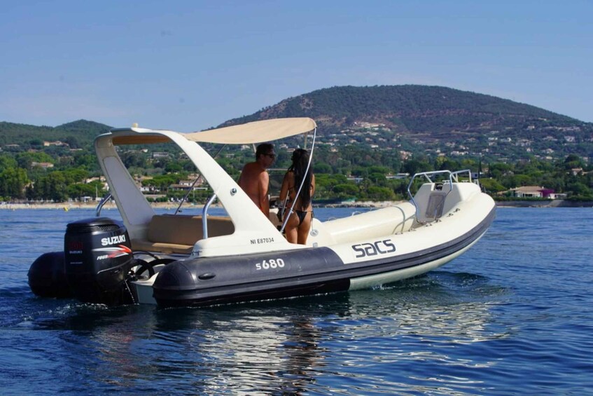 A motorboat with a canopy on the water, a man and a woman on board, and a hilly landscape in the background. 3