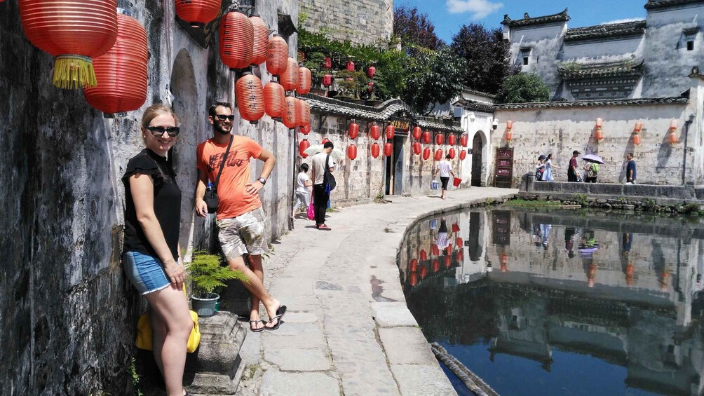 A historic street with red lanterns, a stone wall, and a reflective water body. 3