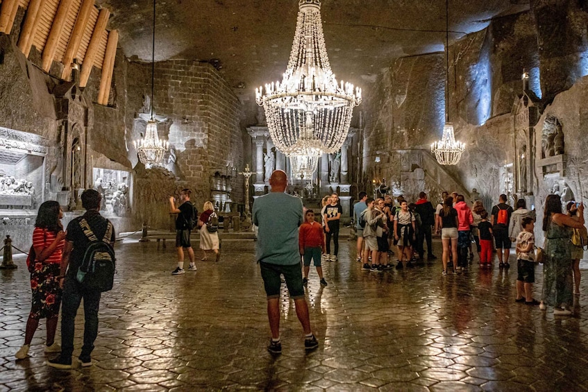 A historic interior with a large chandelier, stone walls, and a crowd of visitors. 1