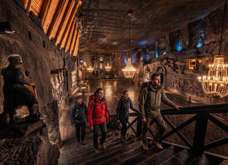 A group of people walking through a dimly lit, historic stone building with wooden railings and chandeliers. 2