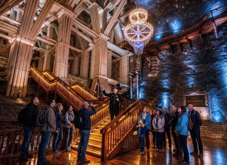 A group of people inside a building with a large, ornate staircase and a chandelier. 1