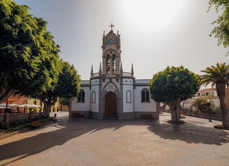 A church with a clock tower, surrounded by trees and a paved square. 1
