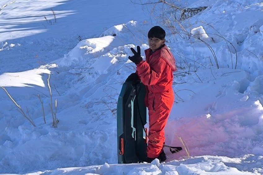Una persona con traje de nieve rojo de pie junto a una tabla de snowboard en un paisaje nevado. 1