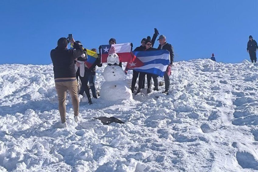 Un grupo de personas en una montaña nevada, con un muñeco de nieve y una bandera. 3