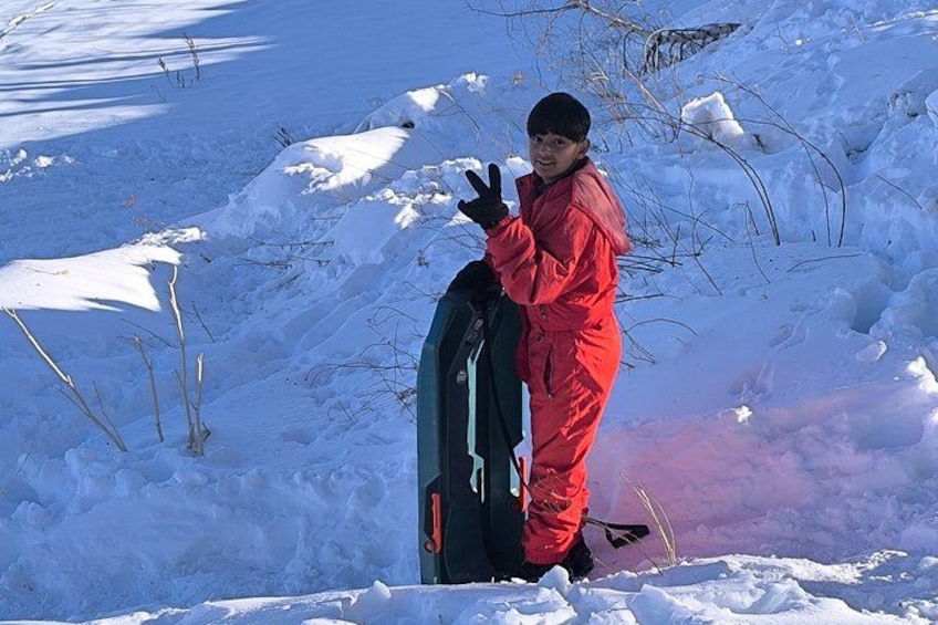 A person in a red snowsuit standing next to a snowboard on a snowy slope. 1