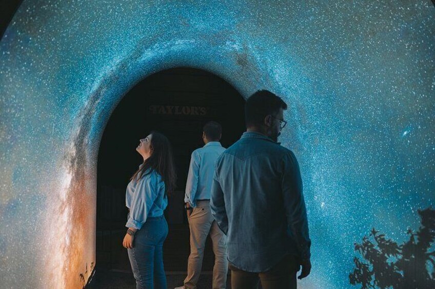 Three people standing in front of a tunnel with a starry sky projected on the walls. 4