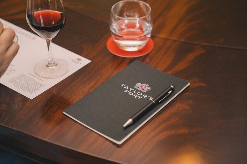 A notebook titled 'Taylor's Port' on a wooden table with a wine glass and a glass of water. 5