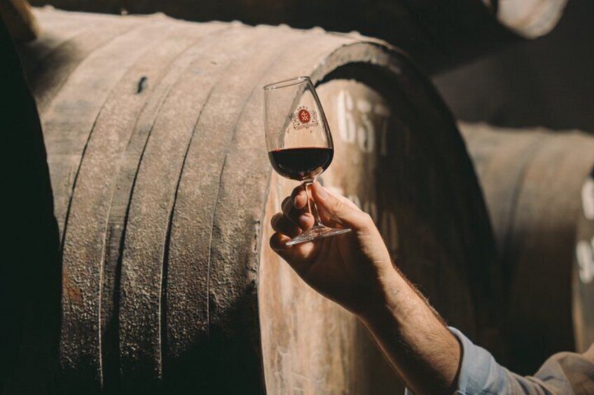 A hand holding a wine glass near wooden barrels. 2