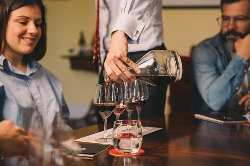A person pouring wine into glasses on a table. 1