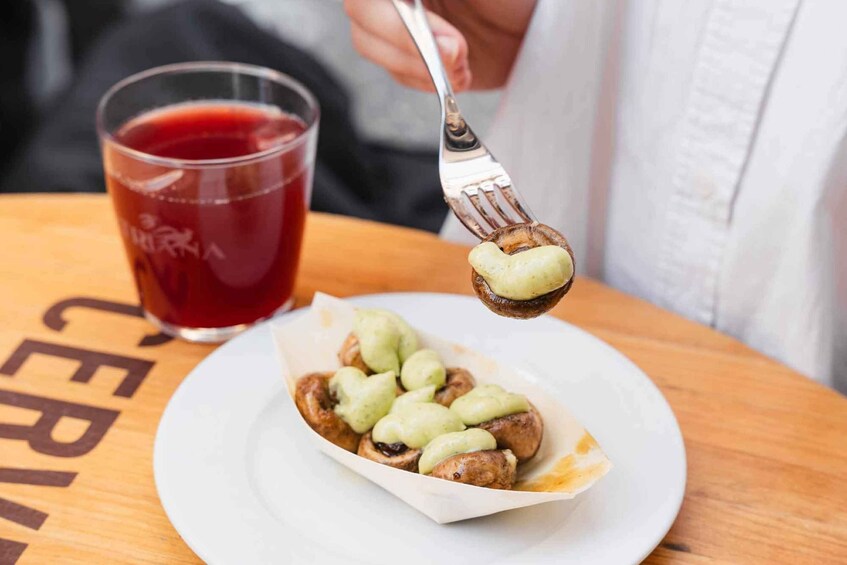A person holding a fork with a food item on it, a glass of red liquid, and a plate with food on a table. 2